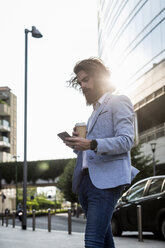 Stylish businessman with cell phone and coffee to go outdoors - MAUF000783