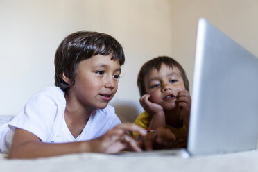 Zwei kleine Jungen liegen auf dem Bett und schauen auf den Laptop - VABF000735