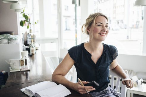 Smiling woman accounting in a cafe - KNSF000200