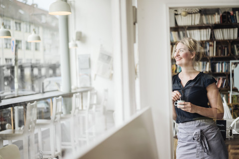 Lächelnde Frau in einem Cafe, die aus dem Fenster schaut, lizenzfreies Stockfoto