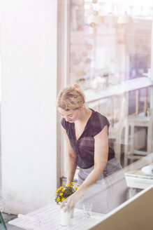 Frau in einem Café legt Blumen auf den Tisch - KNSF000220