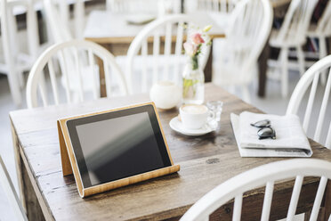 Digitales Tablet, Sonnenbrille, Zeitung und Tasse Kaffee auf dem Tisch in einem Café - KNSF000229