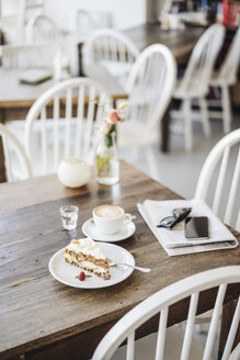 Handy, Sonnenbrille, Kuchen und Tasse Kaffee auf dem Tisch in einem Café - KNSF000230