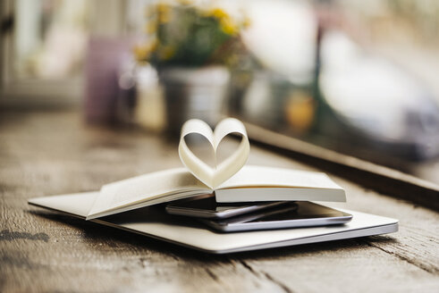 Book with heart-shaped pages on stack of mobile devices - KNSF000243