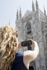 Italy, Milan, back view of tourist taking picture of cathedral with cell phone - MAUF000799