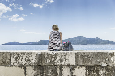 Kroatien, Trsteno, Rückenansicht einer Frau, die auf einer Mauer sitzt und auf das Meer blickt - CHPF000259
