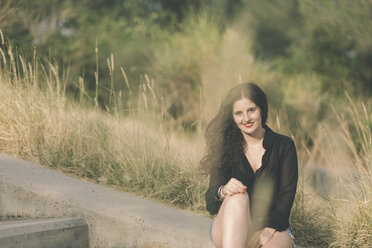 Smiling young woman sitting at wayside - SKCF000159