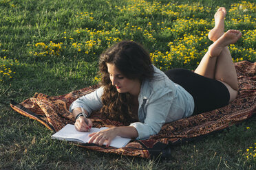 Junge Frau liegt auf einer Decke auf einer Wiese und schreibt etwas in ihr Tagebuch - SKCF000160