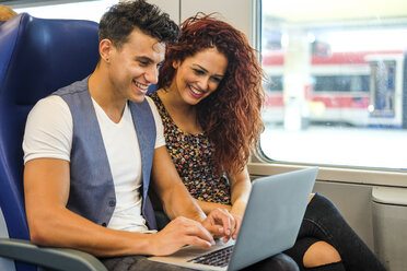 Smiling young couple in a train using laptop - SIPF000766