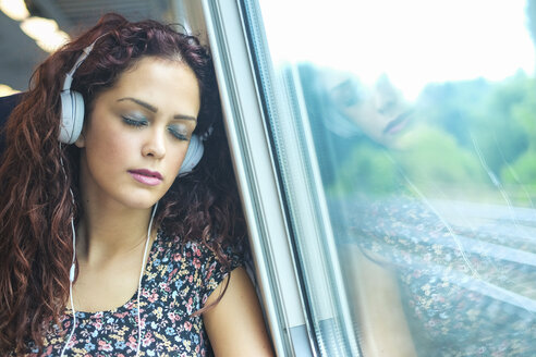 Porträt einer jungen Frau mit Kopfhörern, die sich in einem Zug entspannt - SIPF000769
