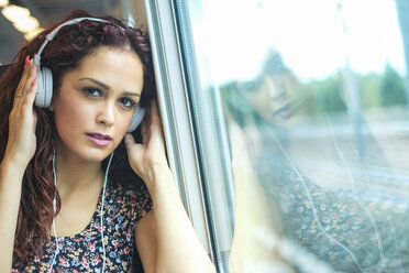 Porträt einer entspannten jungen Frau in einem Zug, die mit Kopfhörern Musik hört - SIPF000770