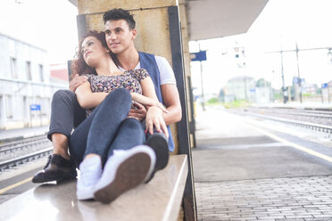Happy young couple sitting on bench on platform - SIPF000773