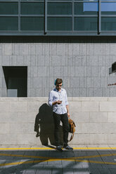 Irland, Dublin, Geschäftsmann mit Kopfhörern, der auf sein Mobiltelefon schaut - BOYF000511