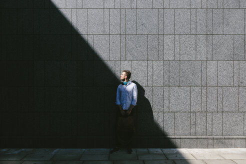 Young businessman standing in front of a grey wall looking up - BOYF000518