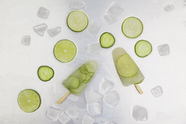 Cucumber and lime ice lollies, ice cubes and slices of lime and cucumber on metal - GWF004863