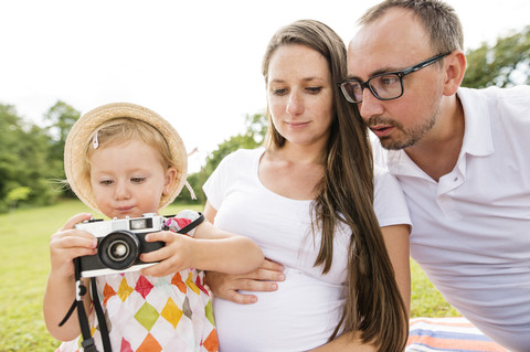 Glückliche Familie im Park, Tochter spielt mit Kamera, lizenzfreies Stockfoto