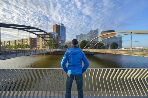 Deutschland, Hamburg, Mann schaut zur Niederbaumbrücke mit Elbphilharmonie und Hanseatic Trade Center am Morgen - RJF000616