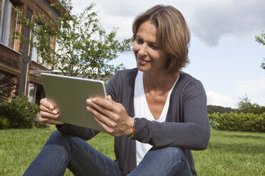 Lächelnde Frau mit digitalem Tablet im Garten - RBF004836