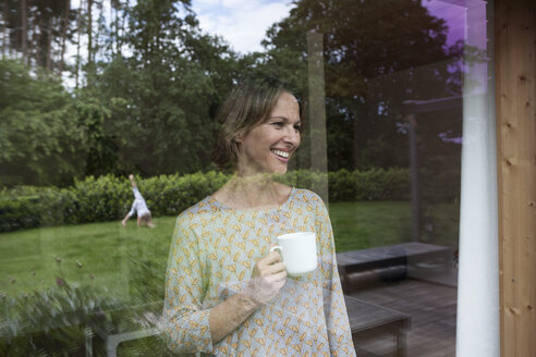 Lächelnde Frau mit Tasse und Blick aus dem Fenster - RBF004845