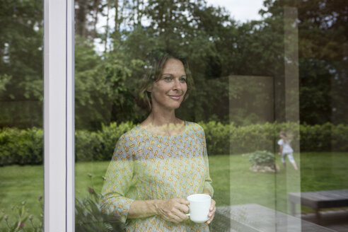 Smiling woman holding cup looking out of window - RBF004846