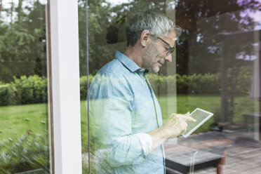 Älterer Mann benutzt digitales Tablet hinter einer Fensterscheibe - RBF004851