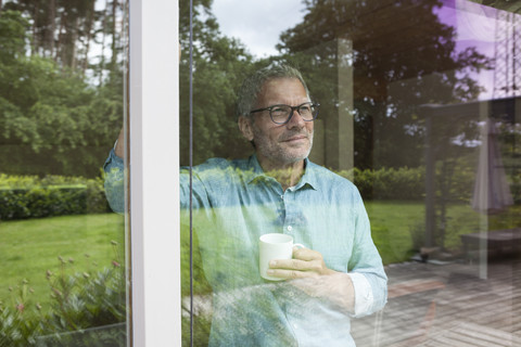 Lächelnder Mann hält Tasse und schaut aus dem Fenster, lizenzfreies Stockfoto