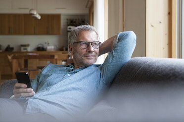 Mature man holding cell phone sitting on couch - RBF004856