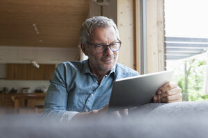 Mature man using digital tablet on couch - RBF004858
