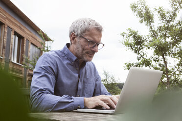 Älterer Mann benutzt Laptop auf Gartentisch - RBF004871