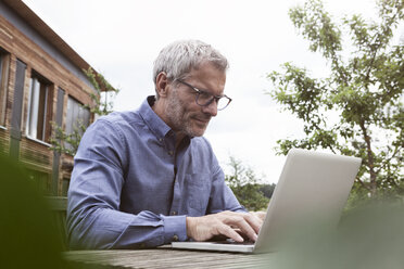 Mature man using laptop on garden table - RBF004871