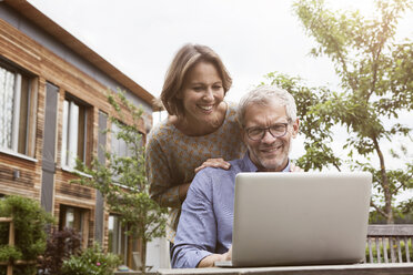 Happy mature couple sharing laptop in garden - RBF004884