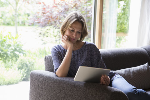 Frau benutzt digitales Tablet auf Couch, lizenzfreies Stockfoto