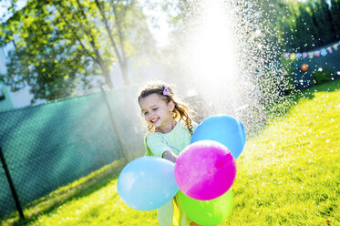 Kleines Mädchen mit Luftballons haben Spaß mit Rasensprenger im Garten - HAPF000770