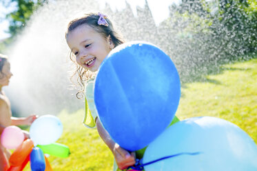 Kleines Mädchen mit Luftballons haben Spaß mit Rasensprenger im Garten - HAPF000771