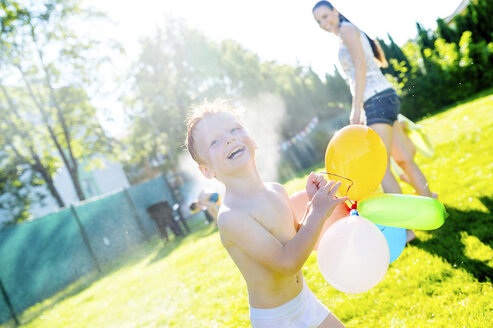 Kleiner Junge mit Luftballons hat Spaß mit Rasensprenger im Garten - HAPF000773