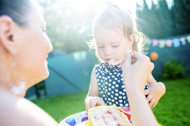 Mutter füttert ihre kleine Tochter mit Kuchen im Garten - HAPF000774