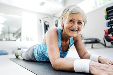 Lächelnde reife Frau auf Gymnastikmatte im Fitnessstudio liegend - HAPF000792