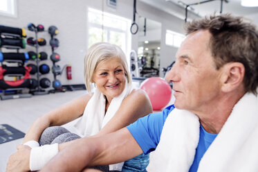 Lächelnde reife Frau und älterer Mann, die eine Pause im Fitnessstudio machen - HAPF000798
