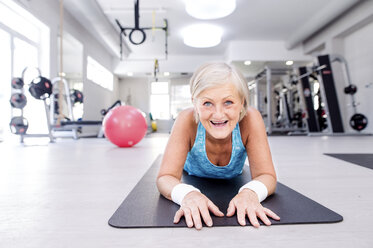 Lächelnde reife Frau auf Gymnastikmatte im Fitnessstudio liegend - HAPF000801