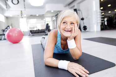 Lächelnde reife Frau auf Gymnastikmatte im Fitnessstudio liegend - HAPF000802