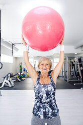 Lächelnde reife Frau, die einen Fitnessball im Fitnessstudio hochhebt - HAPF000816