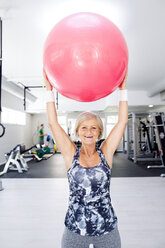 Smiling mature woman lifting up fitness ball in gym - HAPF000816