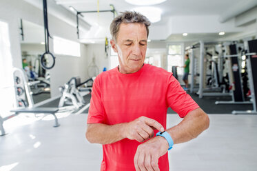 Älterer Mann im Fitnessstudio schaut auf seine Smartwatch - HAPF000835