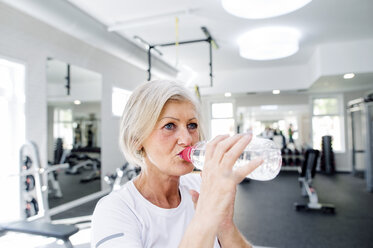 Ältere Frau im Fitnessstudio trinkt Wasser aus einer Flasche - HAPF000838