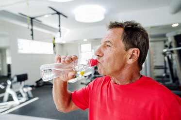 Älterer Mann im Fitnessstudio trinkt Wasser aus einer Flasche - HAPF000839