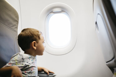 Little boy looking out of window while flying on an airplane - JRFF000836