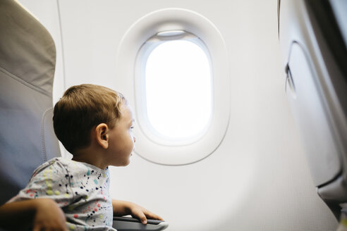 Kleiner Junge schaut aus dem Fenster, während er in einem Flugzeug fliegt - JRFF000836