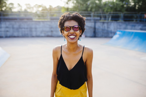 Porträt einer lächelnden jungen Frau mit verspiegelter Sonnenbrille in einem Skatepark, lizenzfreies Stockfoto