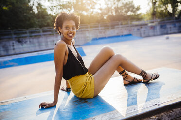 Porträt einer lächelnden jungen Frau, die in einem Skatepark sitzt - GIOF001409