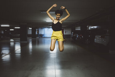 Lächelnde junge Frau, die in einem Parkhaus in die Luft springt - GIOF001414